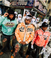 Three men wearing branded jackets in an urban setting with a store in the background.