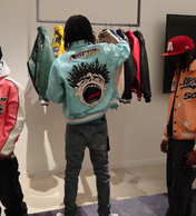 Person wearing a colorful jacket with a graphic design, standing in front of a rack of clothes.