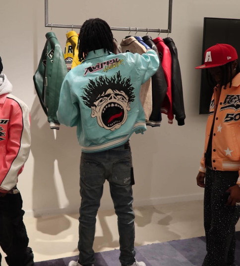 Person wearing a colorful jacket with a graphic design, standing in front of a rack of clothes.