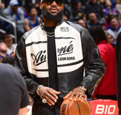 Person wearing a black and white jacket with visible branding, holding a basketball in an indoor setting.