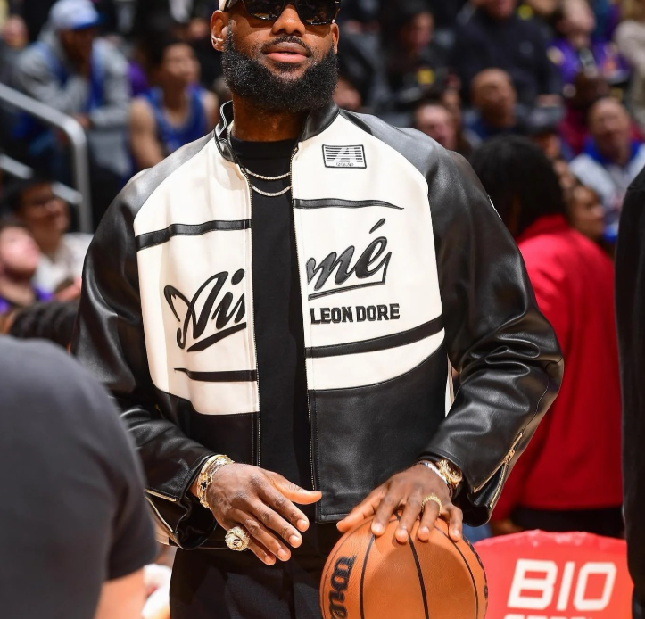 Person wearing a black and white jacket with visible branding, holding a basketball in an indoor setting.