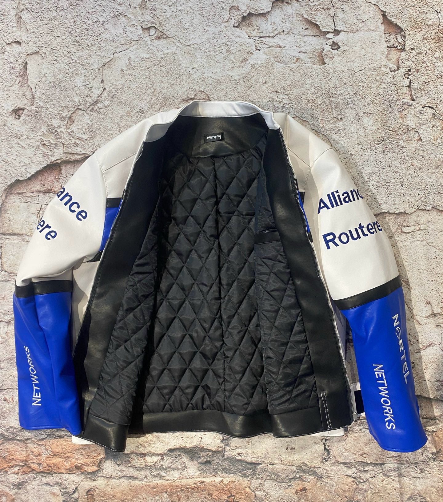 Black quilted jacket with blue and white sleeves against a textured stone wall.