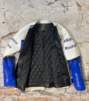 Black quilted jacket with blue and white sleeves against a textured stone wall.