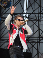 Person on stage with a microphone, wearing a red and white jacket.