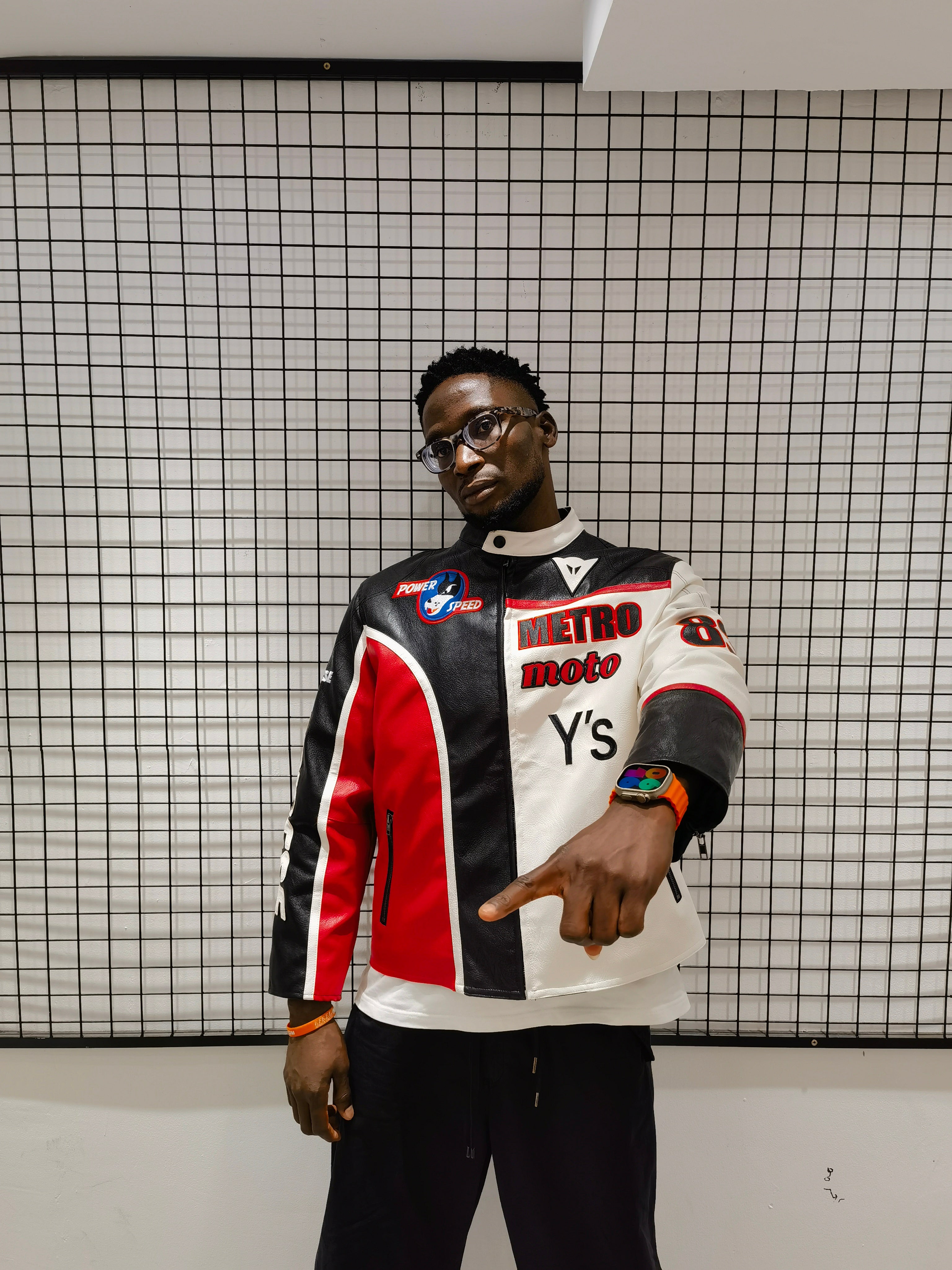 Person wearing a colorful jacket with brand logos against a grid-patterned wall.