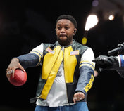 Person in a yellow and black jacket holding a football on a dark background
